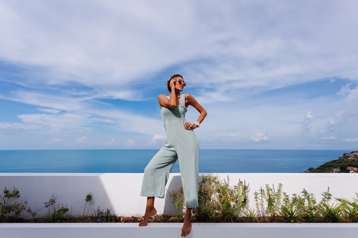 Fit tanned caucasian woman in light blue mint color overall on teracce balcony of luxury villa with amazing tropical sea view
