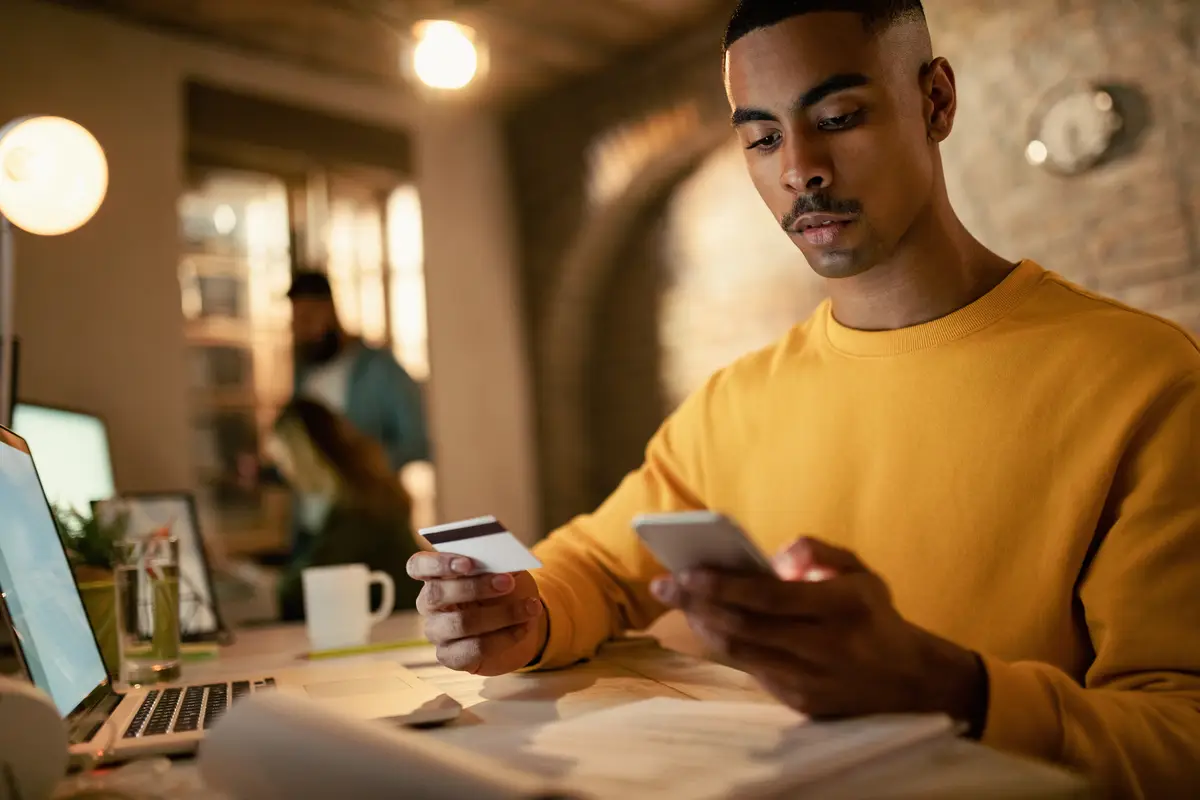 Young black businessman using credit card and smart phone while shopping online in the office