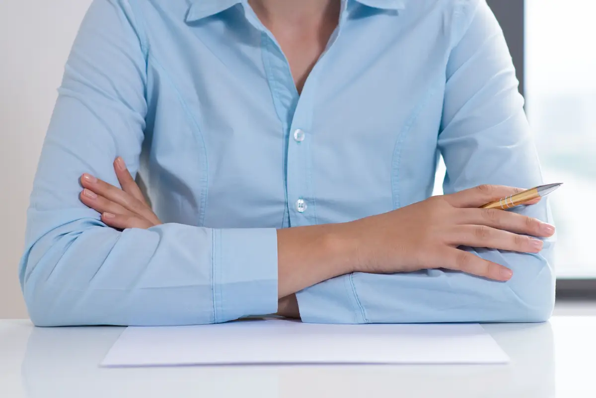 Closeup of woman holding pen and sitting with folded arms