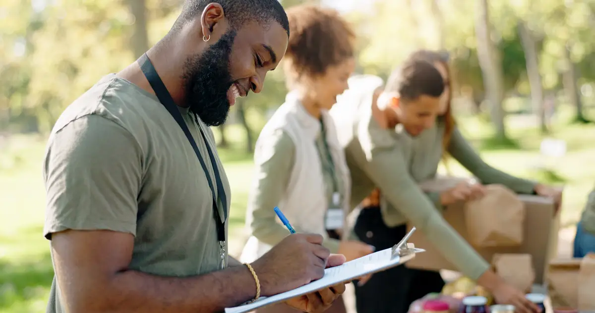 Happy people volunteer and writing with clipboard for checklist on food stock or supplies in charity at outdoor park Man and team working together for NGO mission or community service in nature