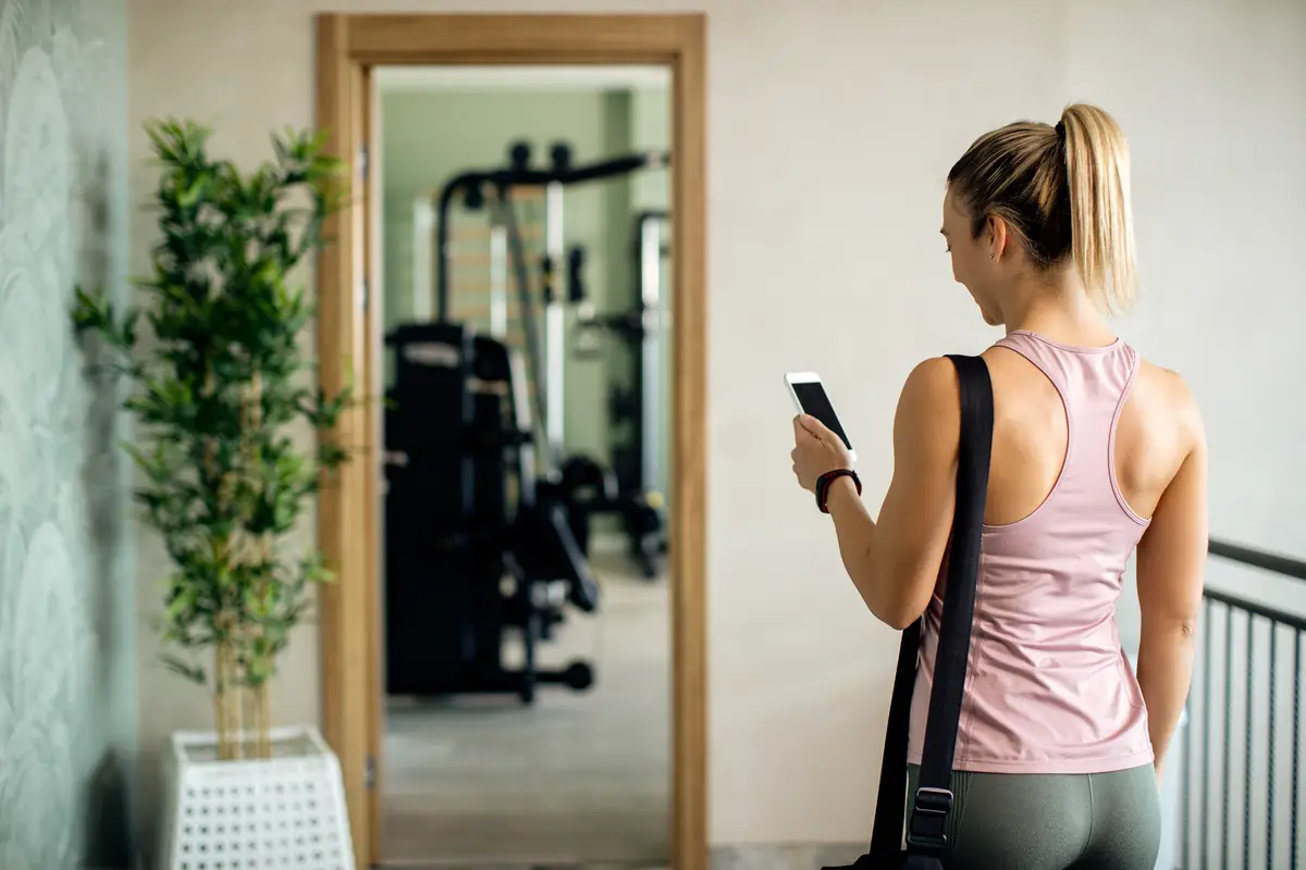 Rear view of athletic woman texting on the phone in a hallway at the gym