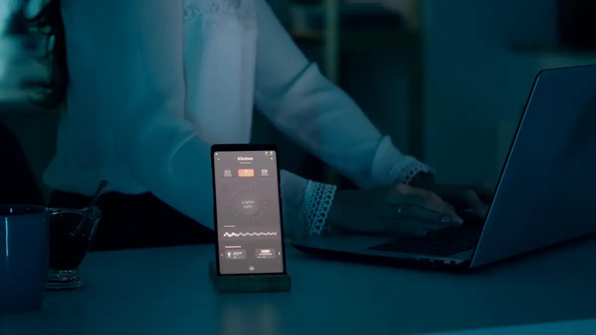 Woman typing at laptop sitting in home with automation lighting system using voice controlled on sma...