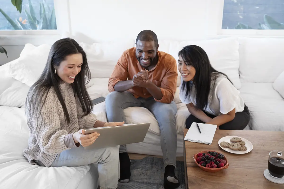 Group of young people using laptop together at home on sofa and having snacks