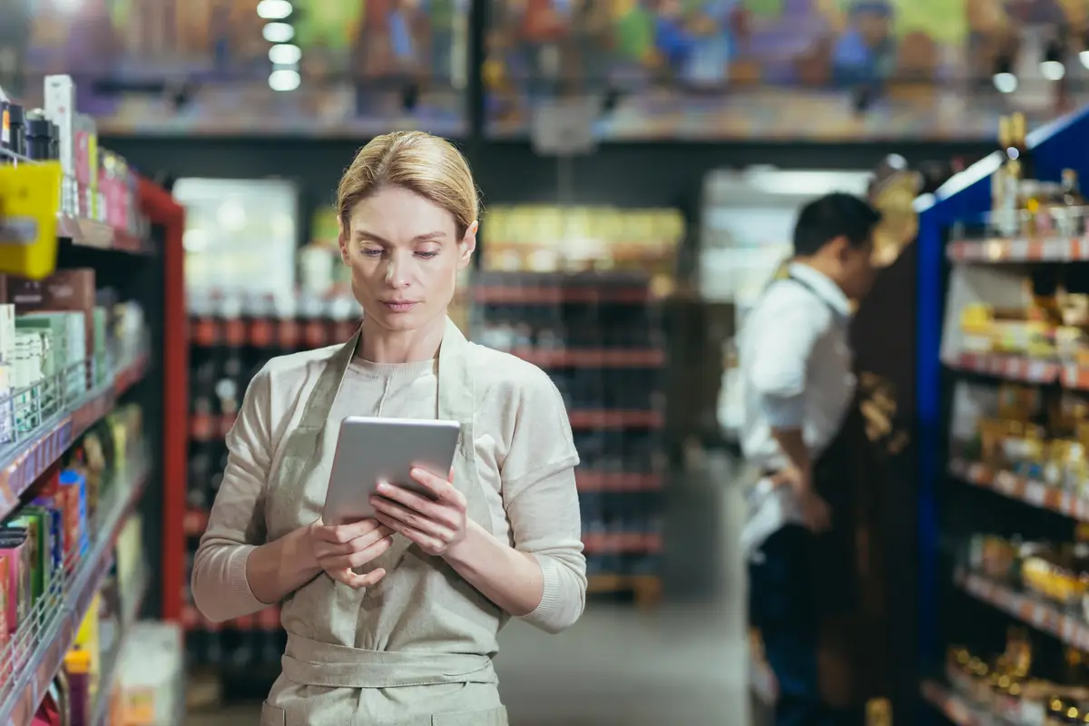 A woman seller in a supermarket uses a tablet computer to count the remaining goods colleagues