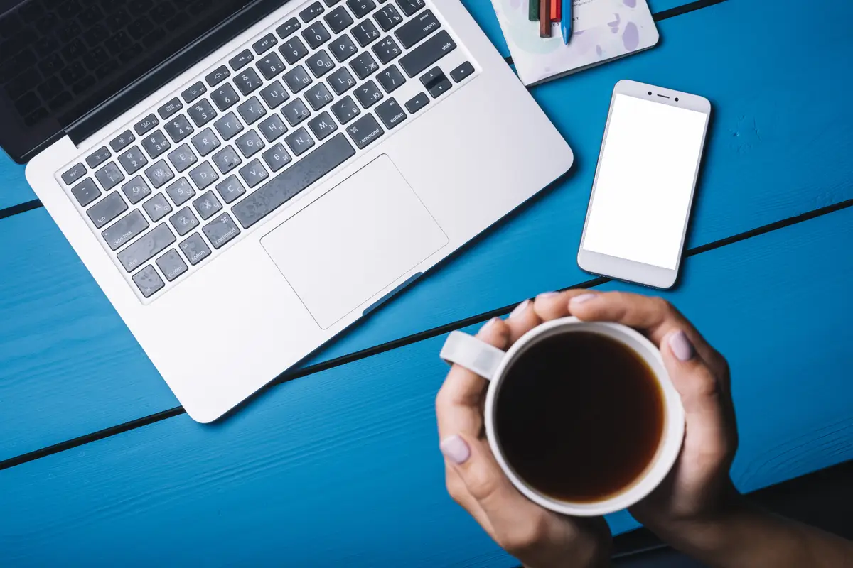 Laptop and smartphone on blue desk with coffee