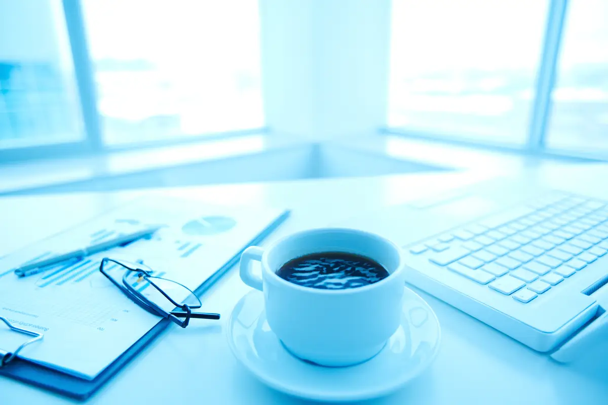 Close-up of cup of coffee with laptop and glasses