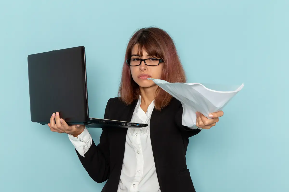 Front view female office worker in strict suit holding laptop and files on blue surface