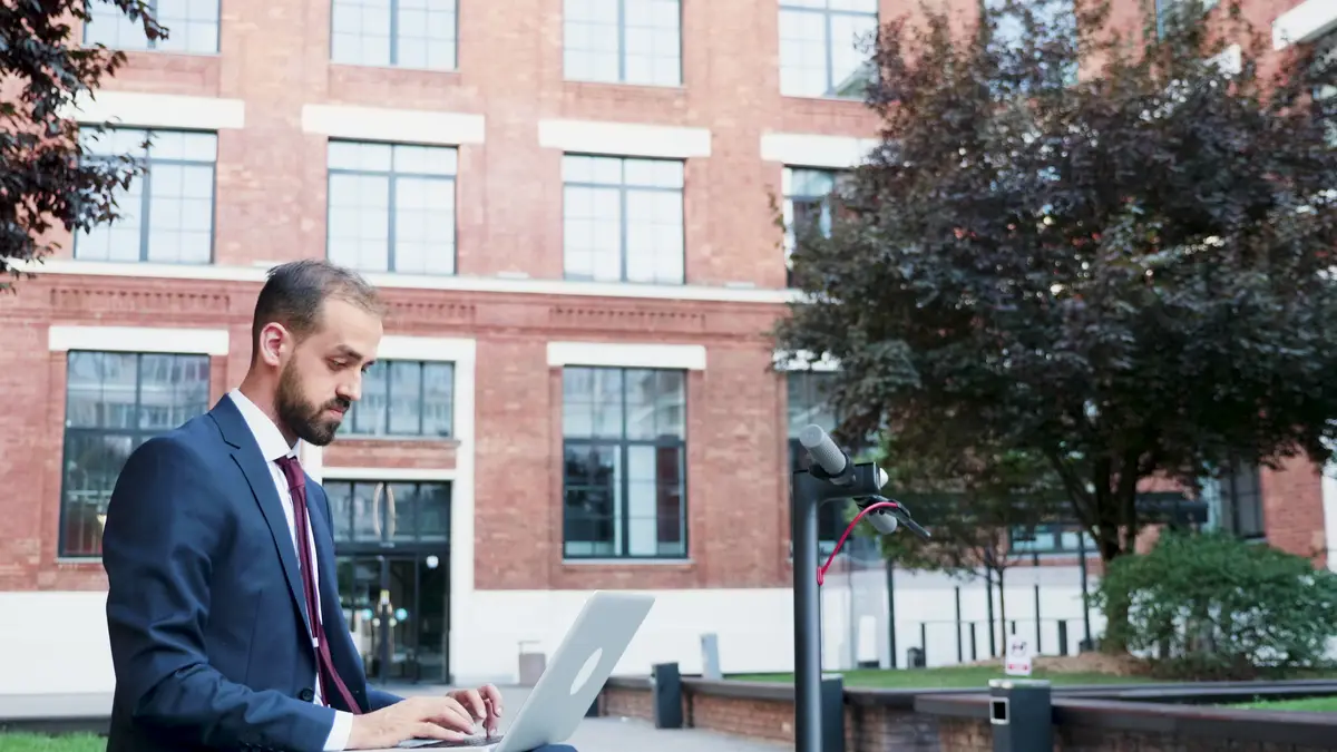 Successful businessman in suit working at marketing presentation sitting on bech outside in front of corporate building office. Executive manager searching information on internet.