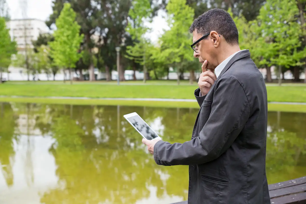 Pensive man using tablet and standing in city park