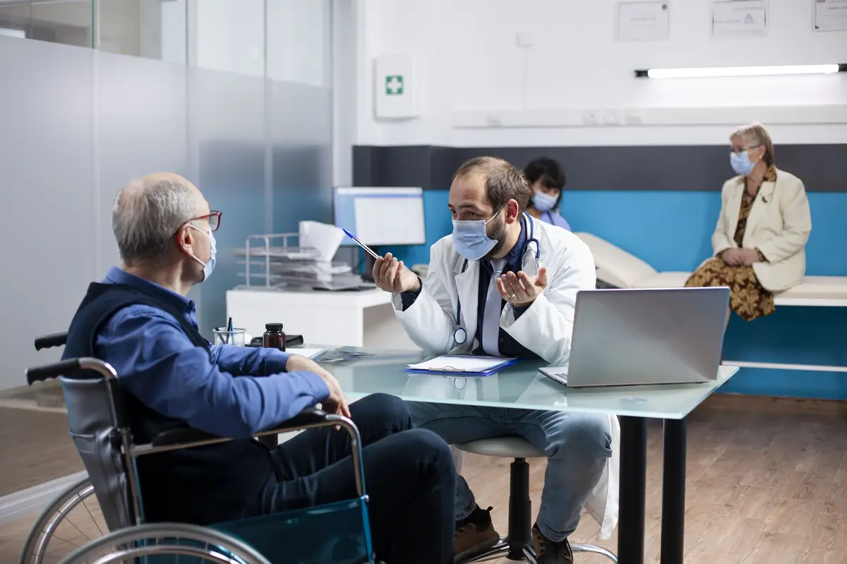 Doctor talks to old patient in wheelchair
