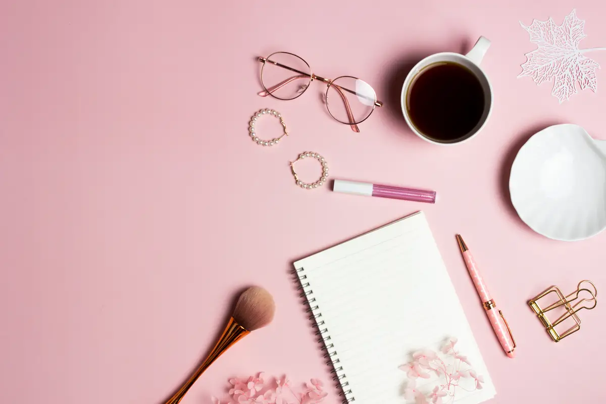 Women items concept with notebook coffee cup envelope and make up over the pink background