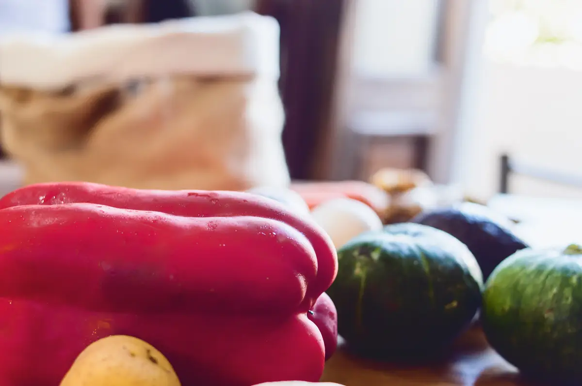 Closeup of a red bell pepper with other fresh vegetables on a table inside a house