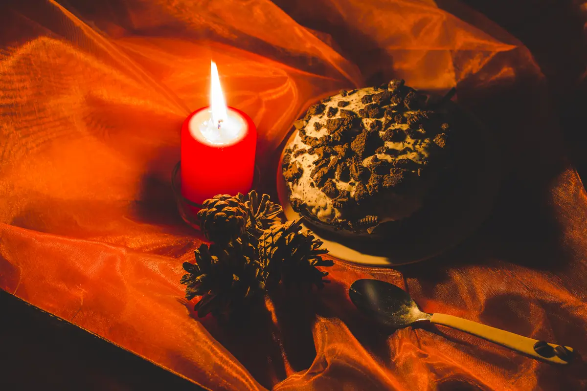 Cake; lit candle and pinecones with spoon on red clothes