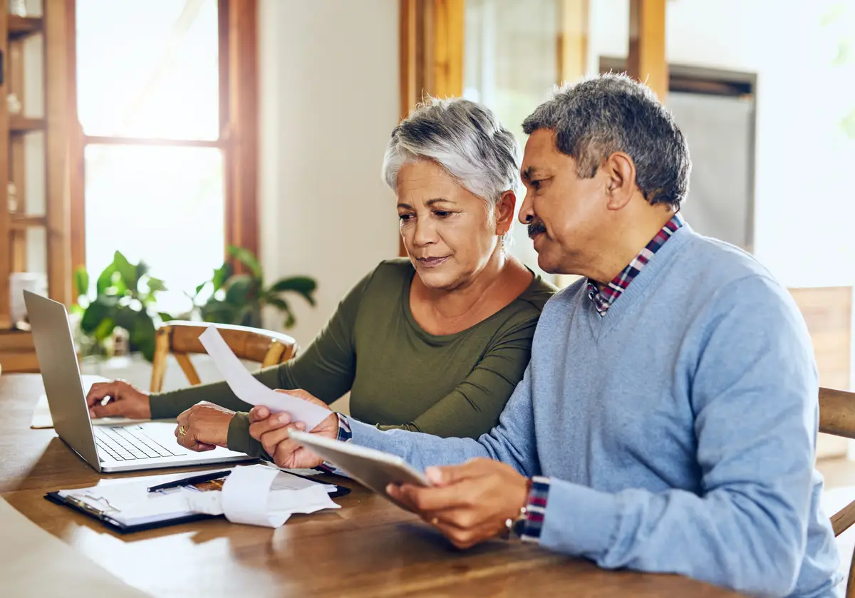 Senior couple budget planning and health insurance checklist with computer at home Documents pension and elderly people with financial tax and debt form in a house with bills and pc admin