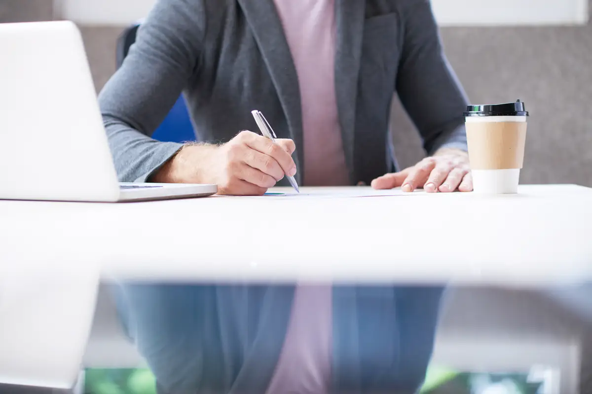 Unrecognizable man sitting at desk in office and writing