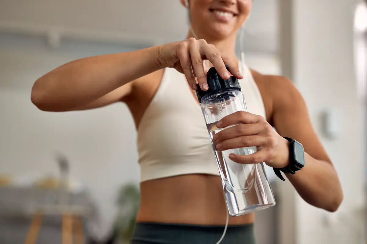 Closeup of thirsty female athlete opening water bottle at home