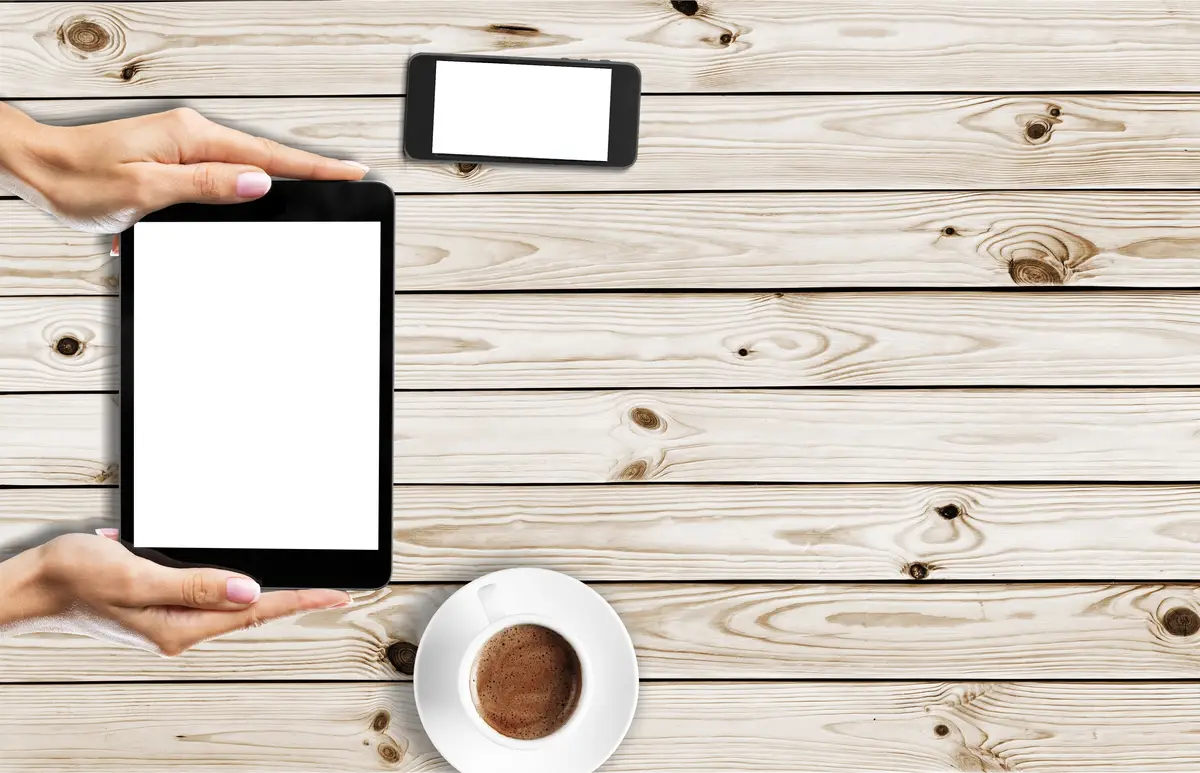 Human hands Holding digital tablet with blank screen with phone and coffee on table background