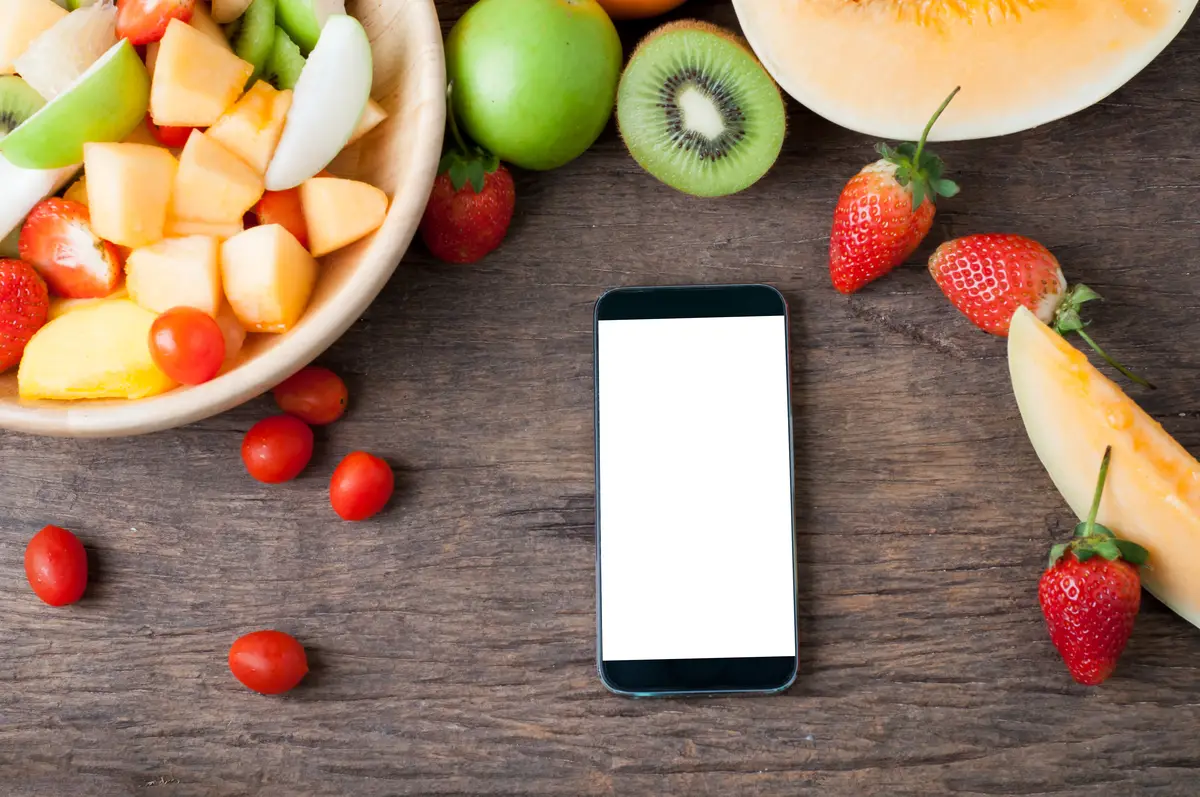 kitchen table with blank screen on smart phone and fruits salad.