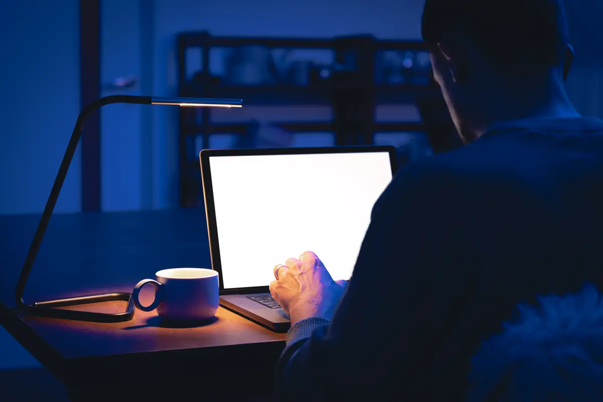 A man works in a dark room uses a laptop at night