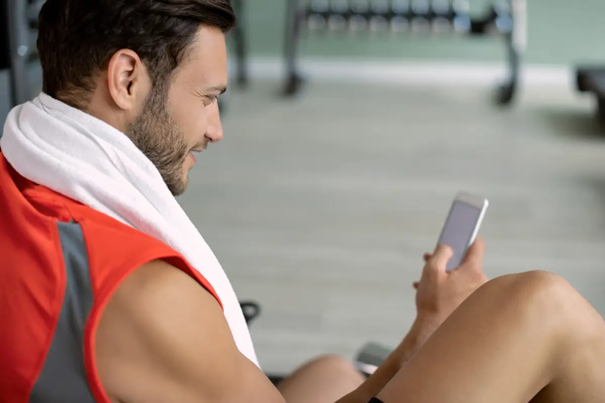 Happy athlete typing text message on mobile phone in a gym