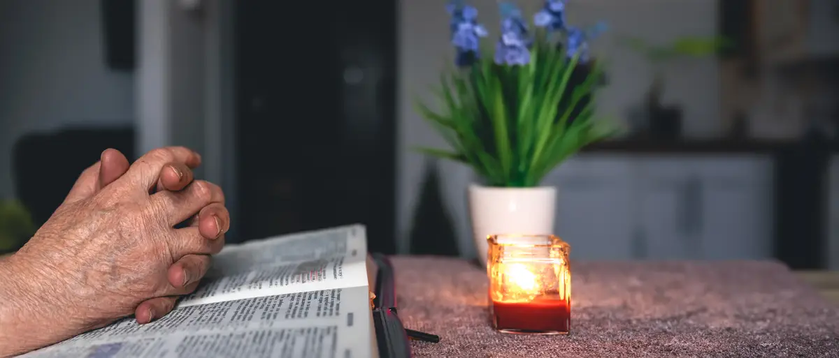 Hands folded in prayer on a Holy Bible in church concept for faith