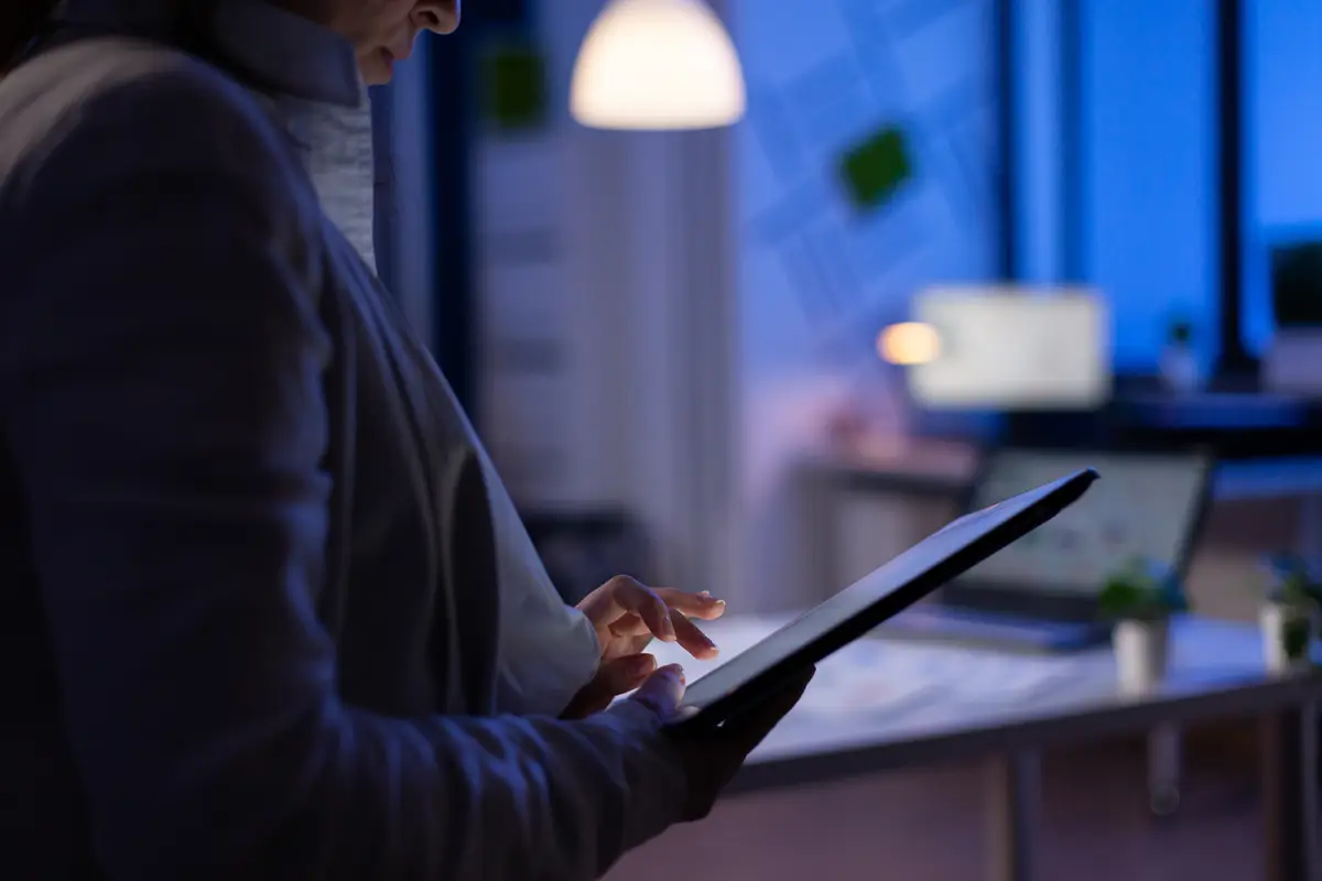 Close-up of woman hands typing on tablet checking financial graphs standing in start-up office late at night