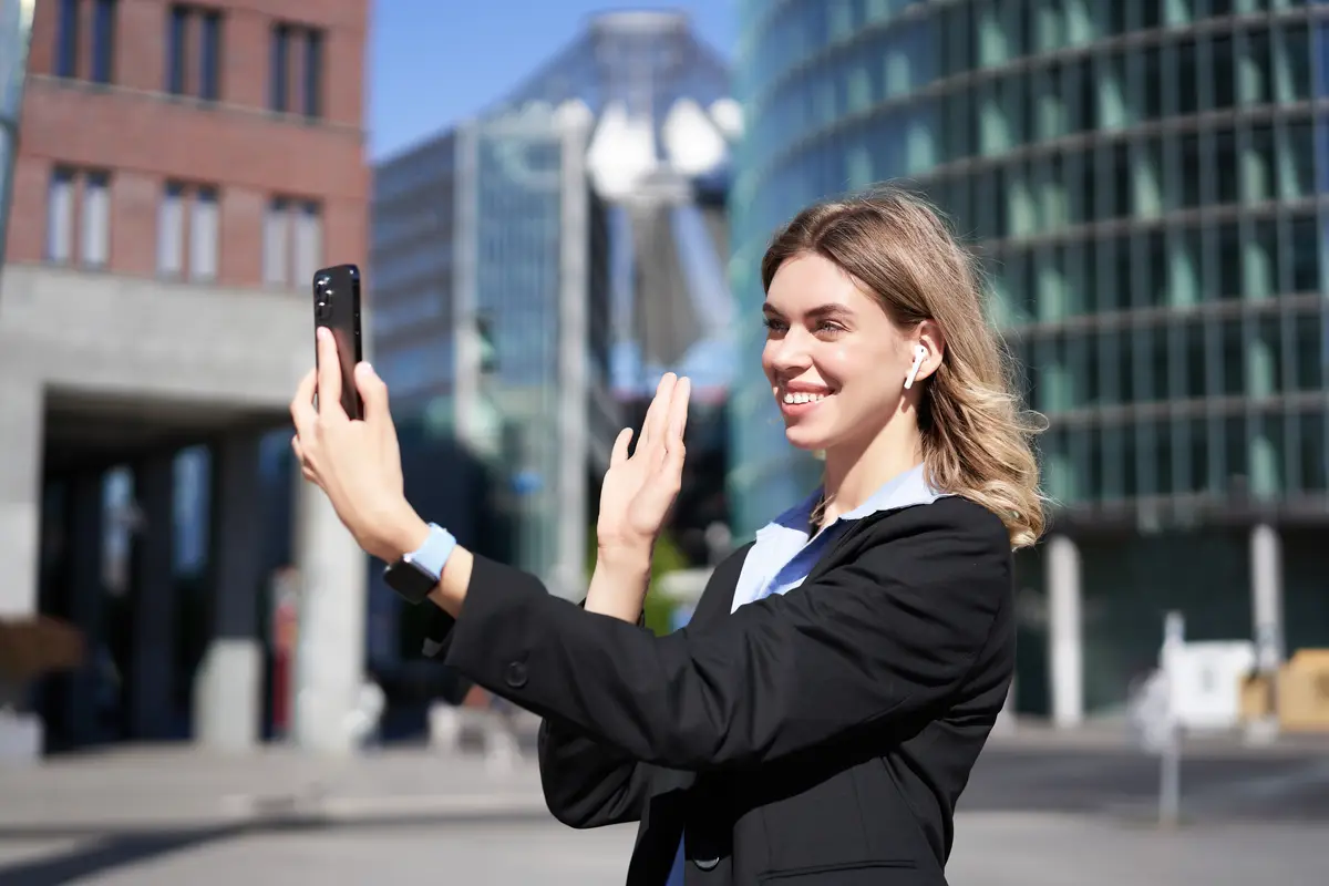 Portrait of businesswoman wave her hand at mobile phone camera waves hand during video chat stands i