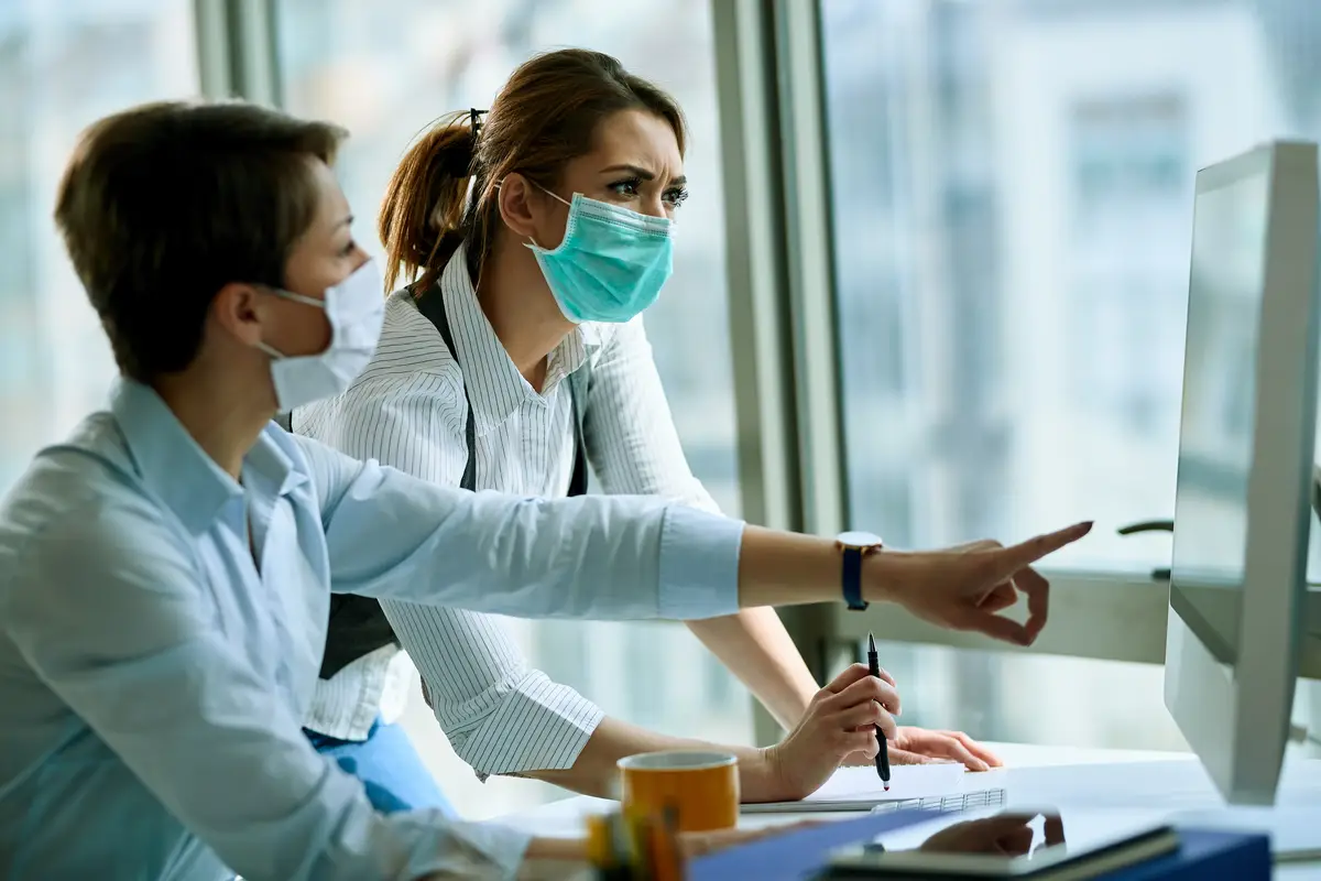 Importância da consulta formal no tratamento da bacteremia por Staphylococcus aureus 3 Young businesswoman and her colleague wearing face masks while working on a computer in the office during virus epidemic