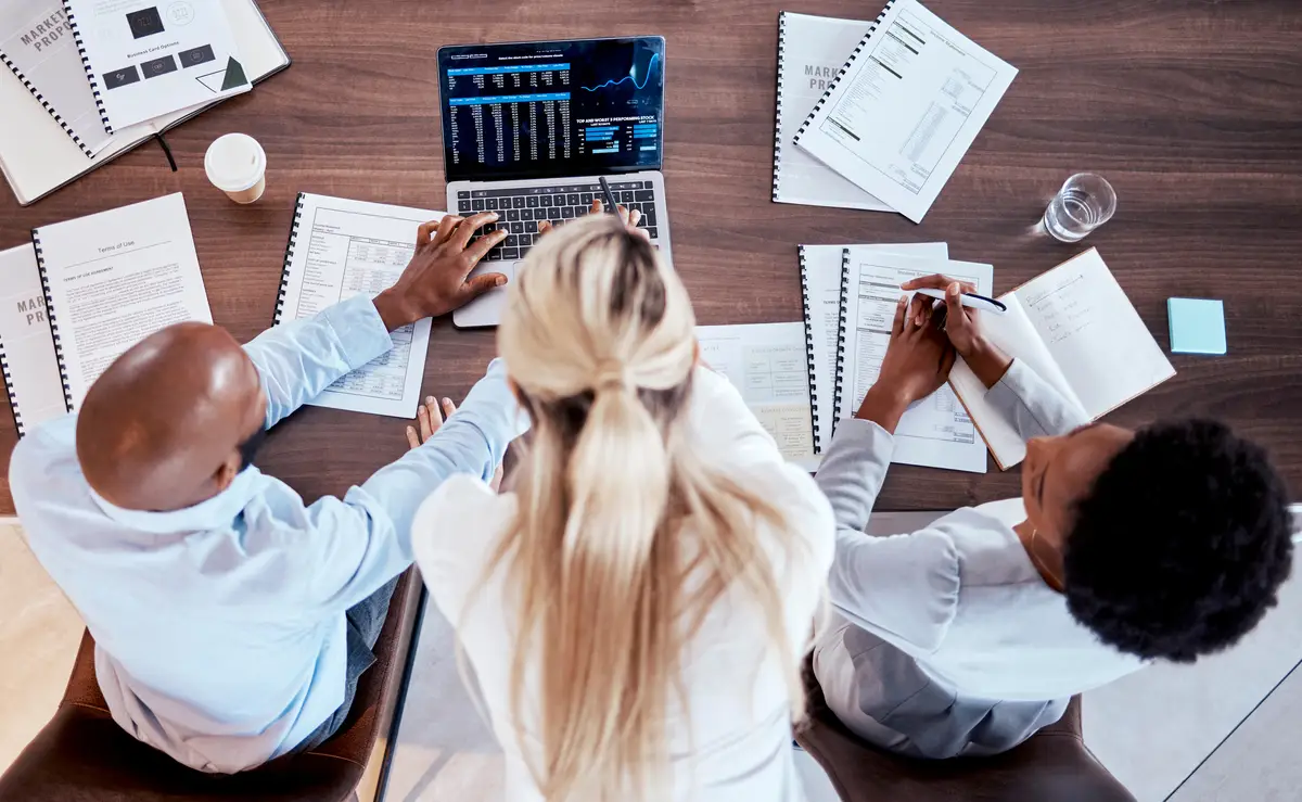 Investment collaboration and laptop with business people in office for stock market trading or data Growth chart and finance with top view of employee and review for economy documents or digital