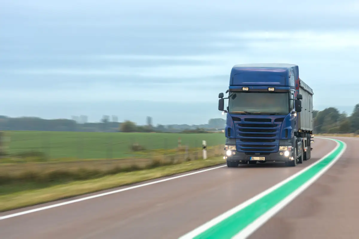 Blue truck on rural highway with green line logistics in motion