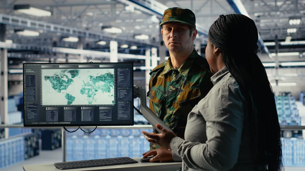 Team of military specialists in data center looking at world map on screen coordinating mission