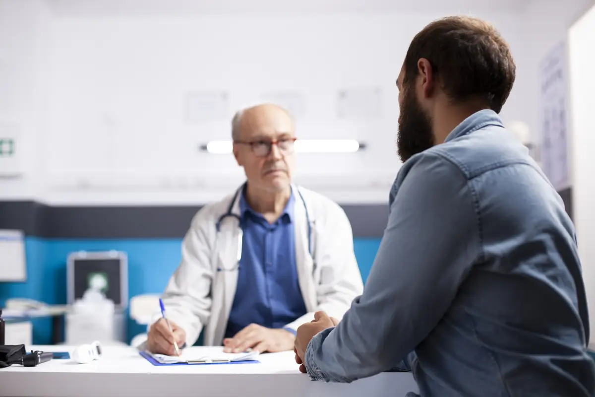 Old physician listens to man in clinic