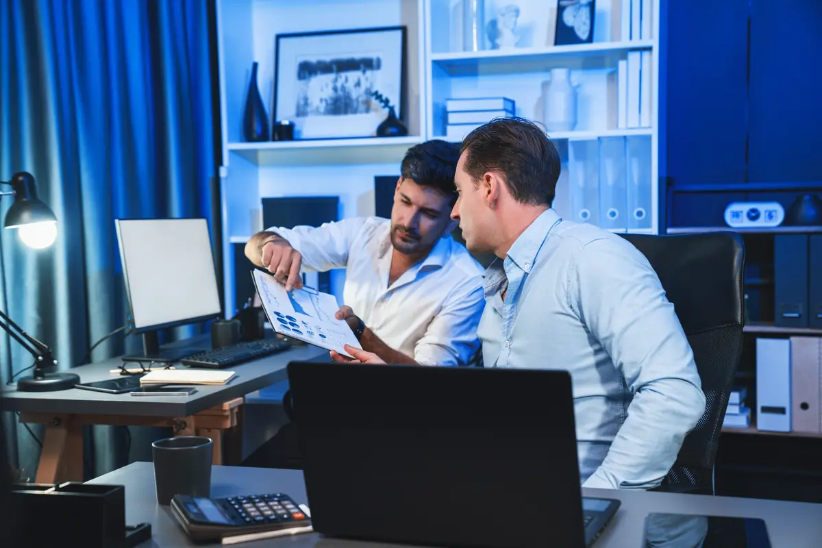 Business partners focusing on document sheet work at night time in modern office analyzing on creative project at blue neon decorative room Concept of brainstorming new stratup company Sellable