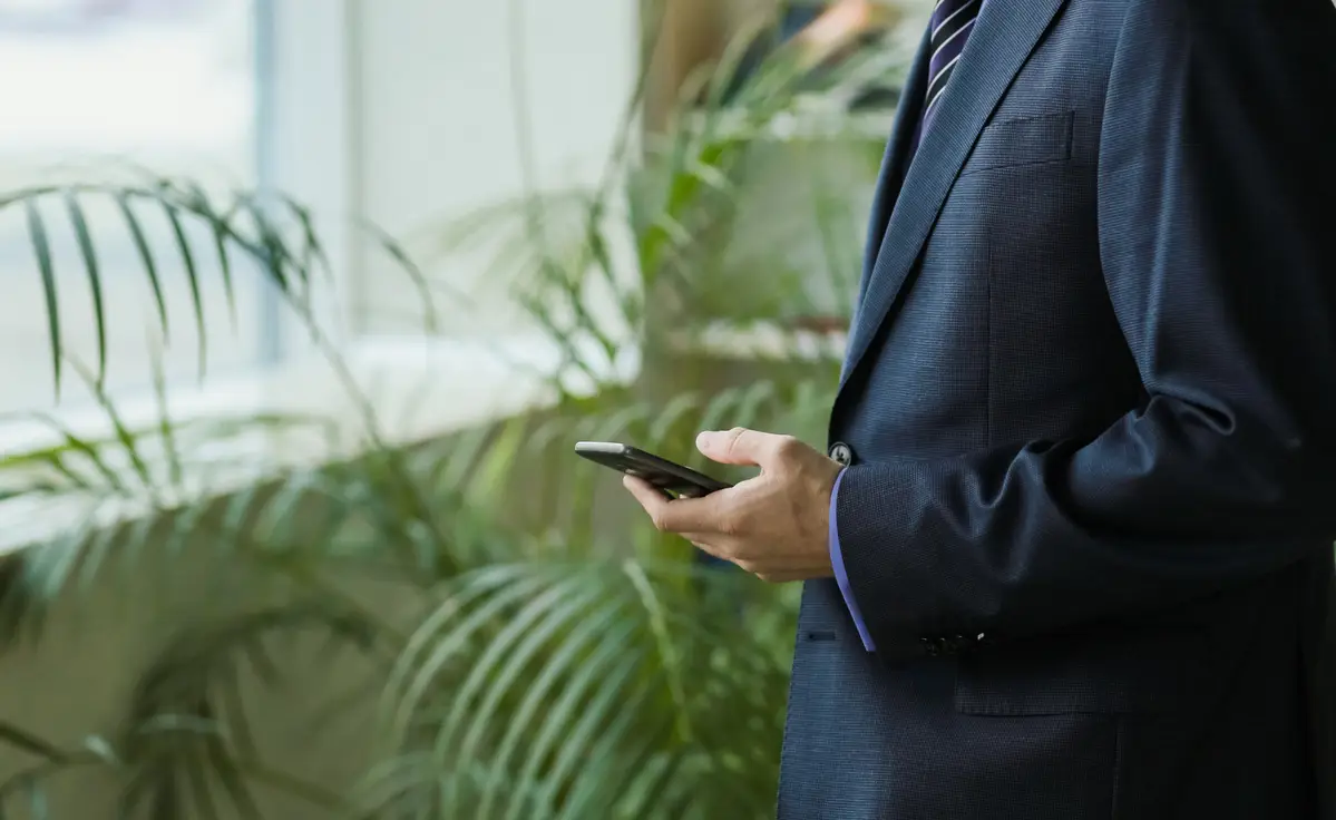 male office worker in suit with smartphone near window and palm trees