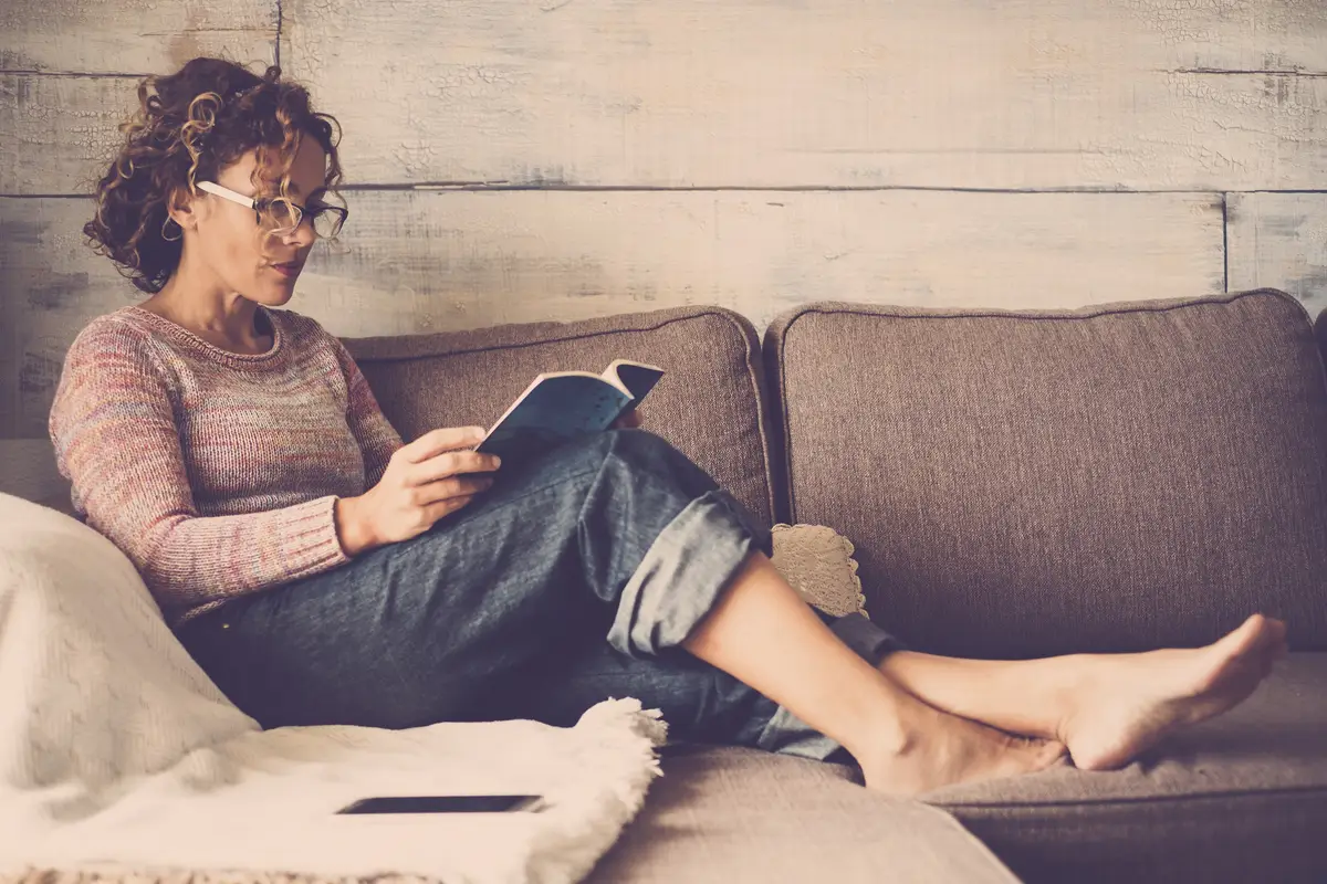 Young woman reading book while relaxing on sofa at home