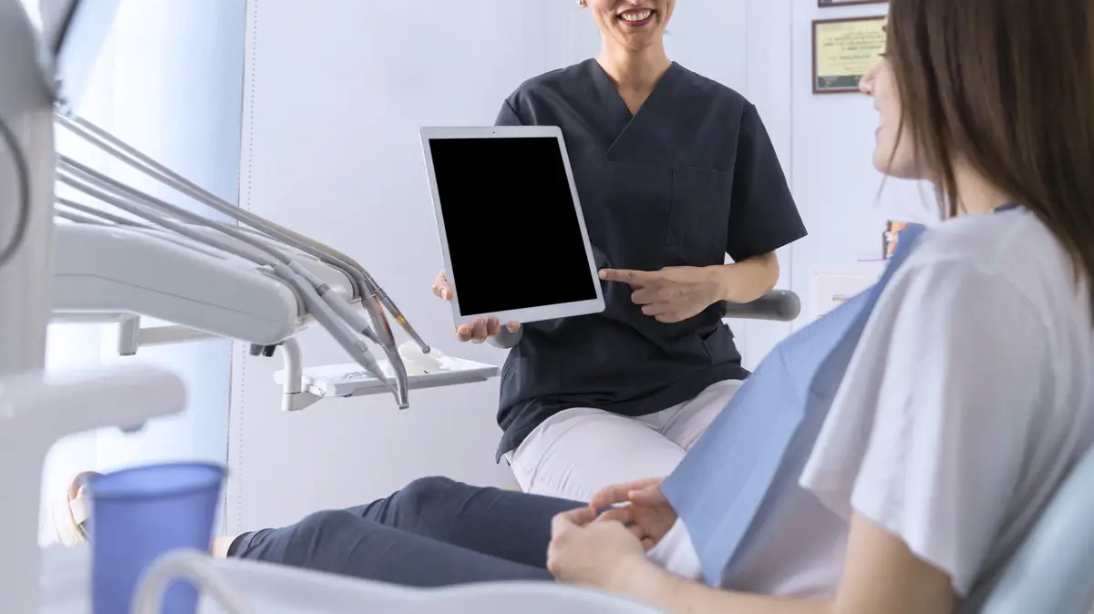 Dentist pointing on digital tablet screen to female patient sitting on chair