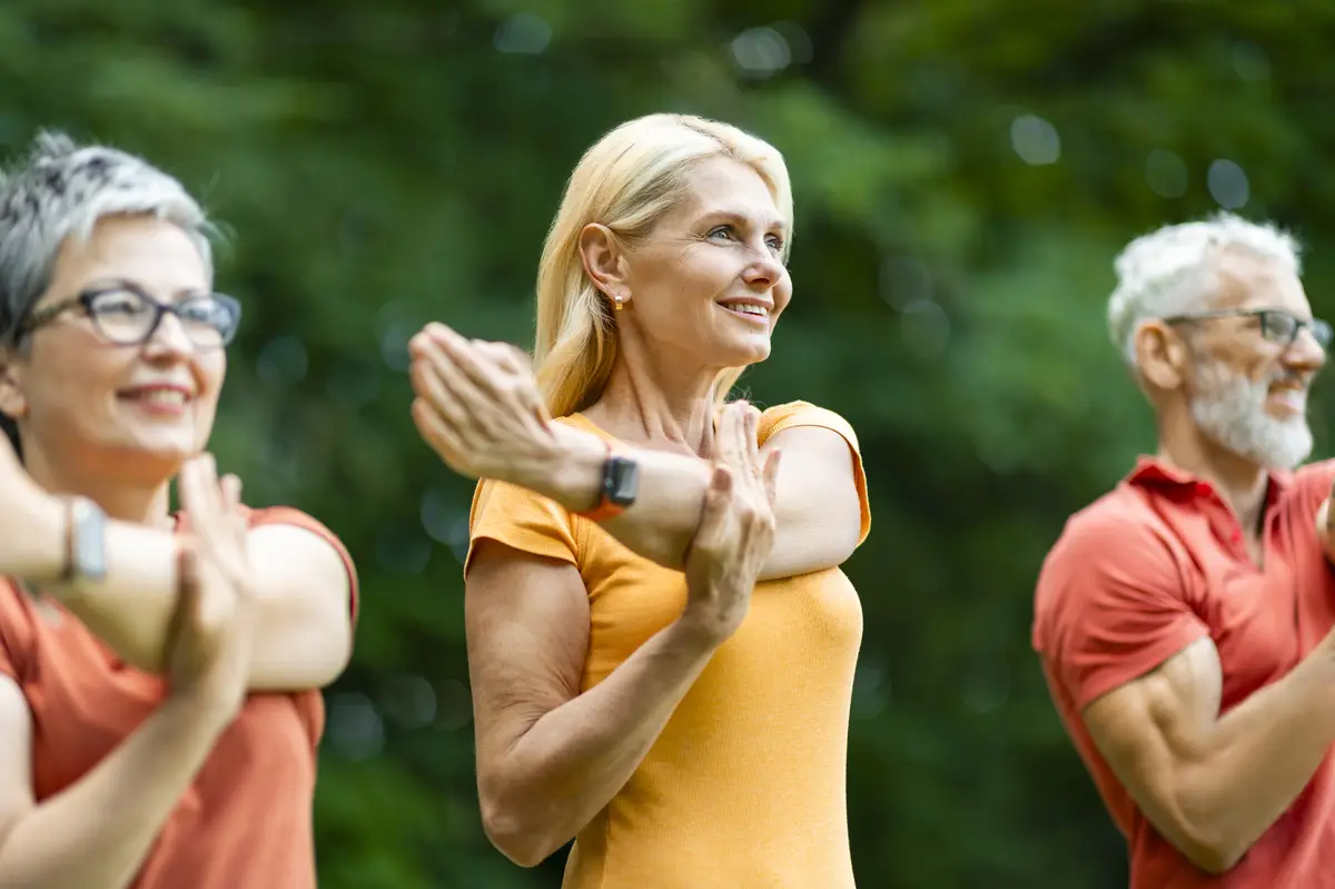 Group of happy senior people training outdoors stretching arm muscles