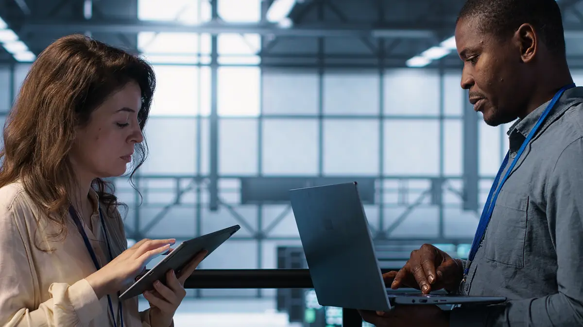 Team of technicians working in server farm using laptops to analyze data