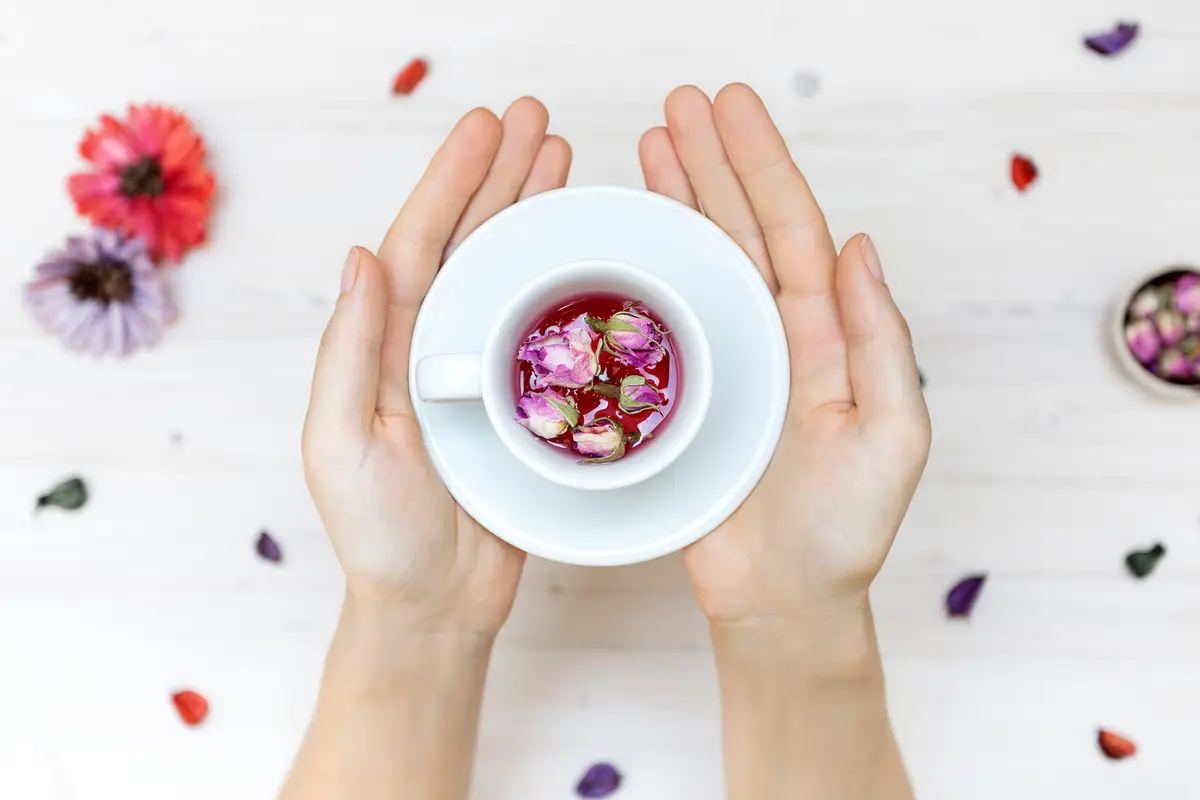 person holding a white teacup with rose petals