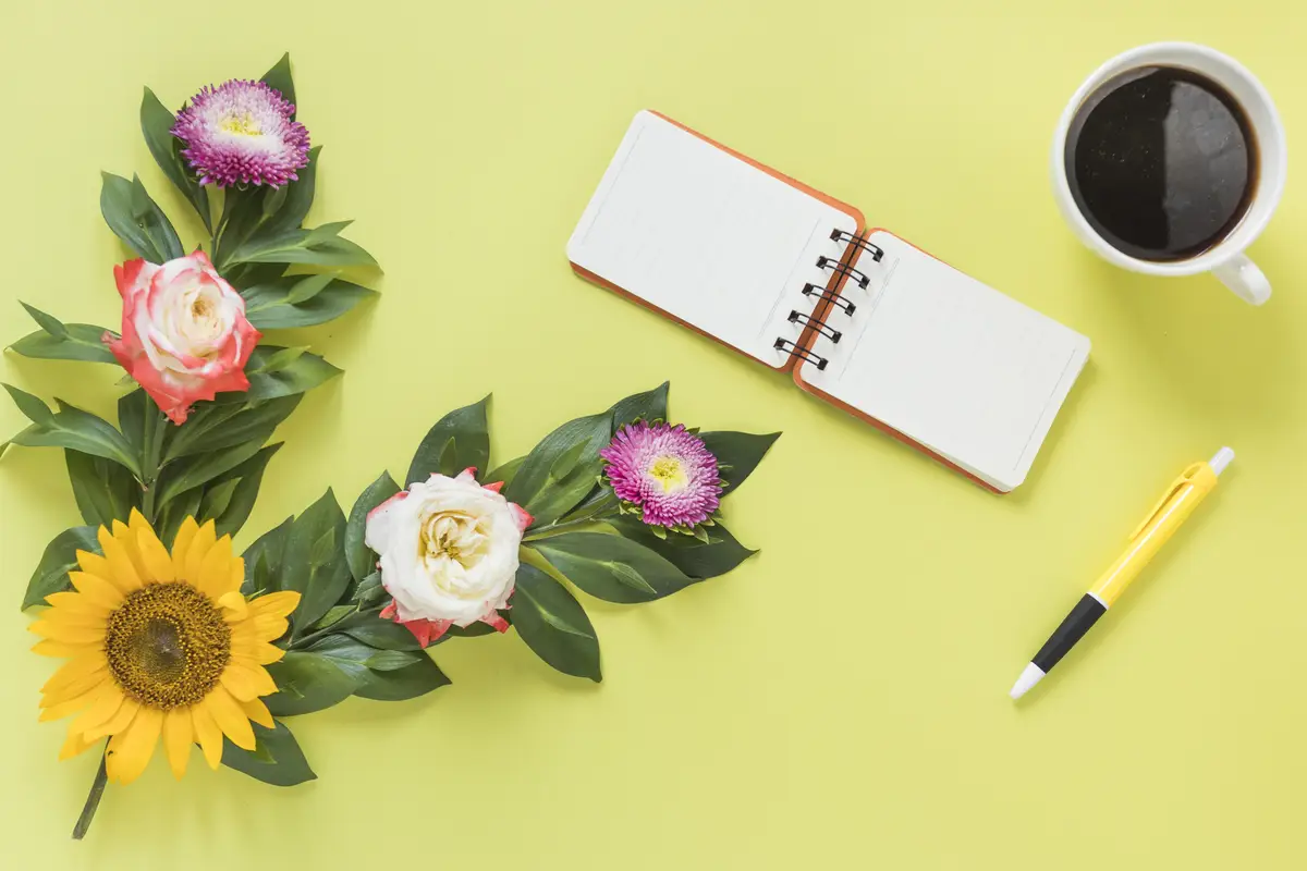 Spiral notepad; black tea; pen and flowers on colored background