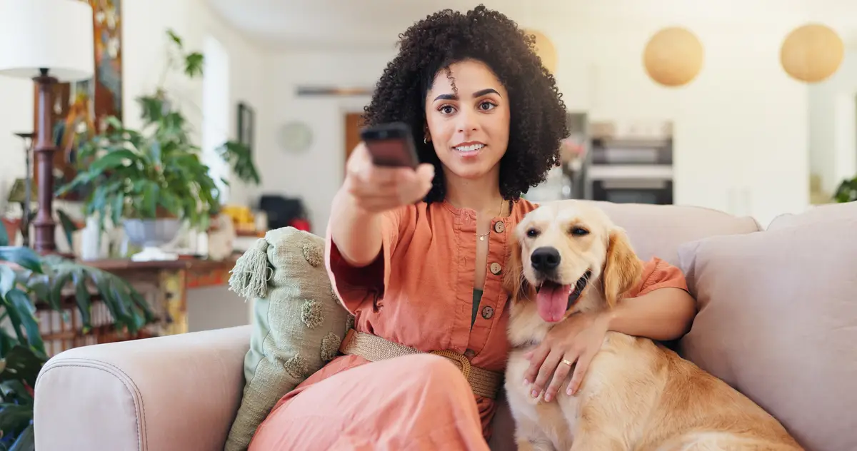 Woman remote and relax with dog for watching tv change channel and streaming movie in lounge Female person hug and labrador puppy for online series film and subscription of entertainment on sofa