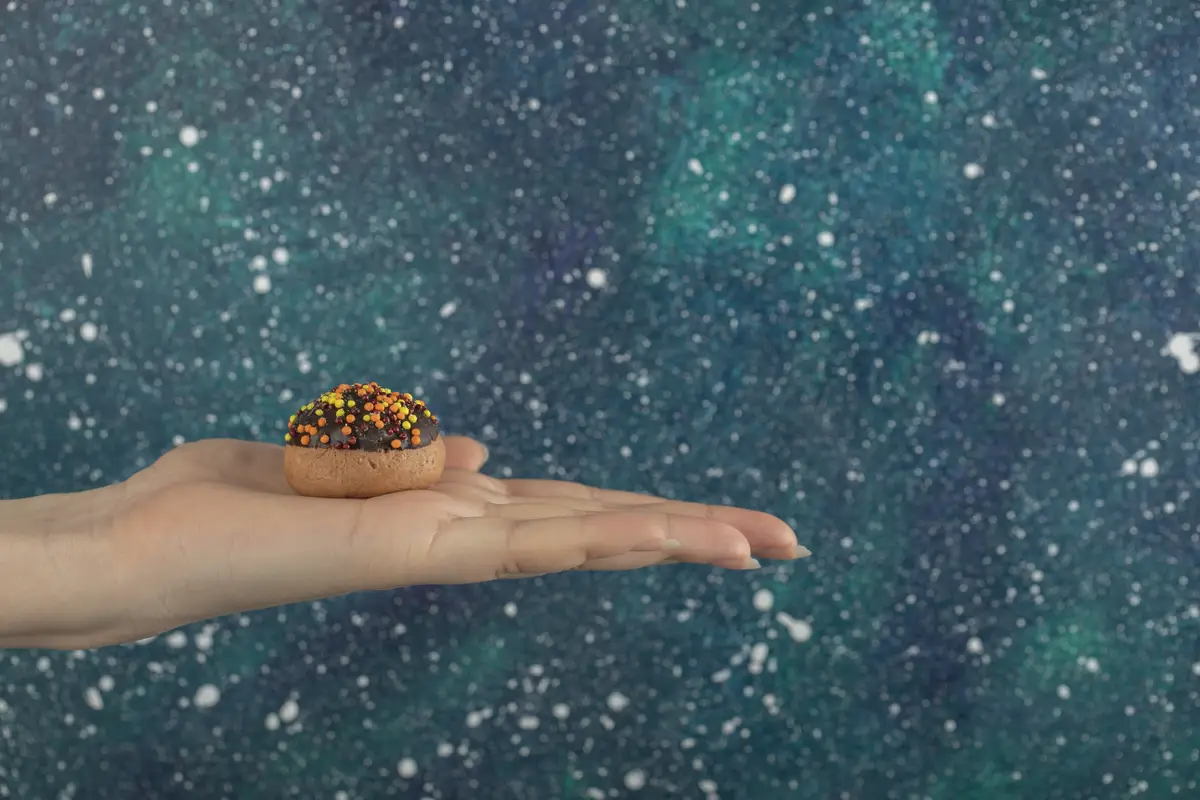 Female hand holding cookie on colorful surface.