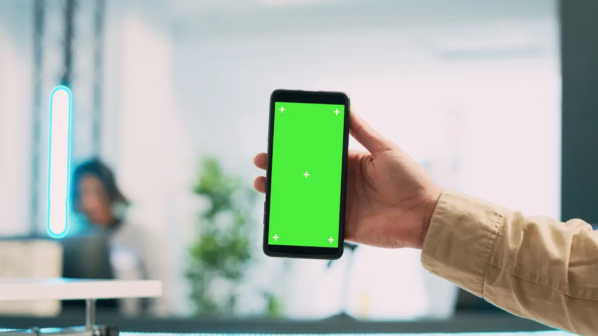 Young employee using mobile phone with green screen, showing isolated copyspace display on smartphone. Male store assistant holding blank chroma key mockup template in boutique. Close up.