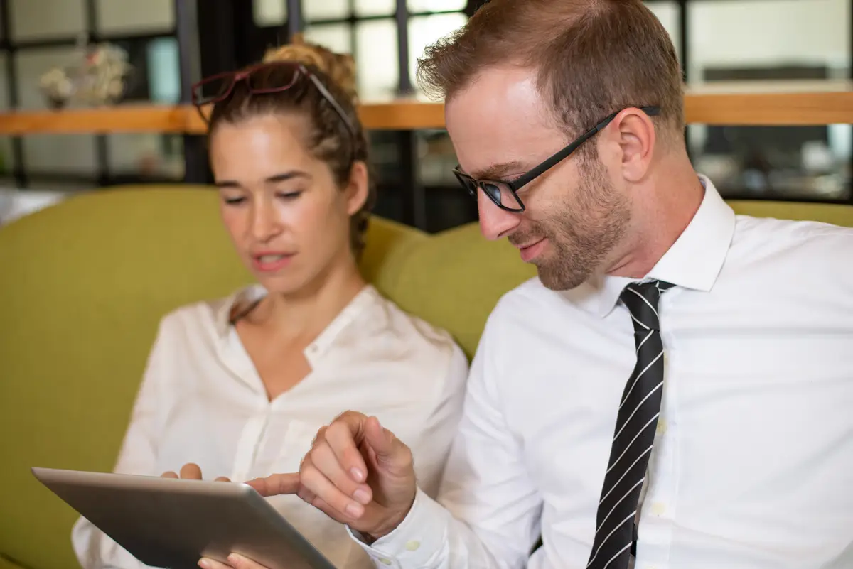 Relaxed coworkers chatting and using tablet in office lobby.