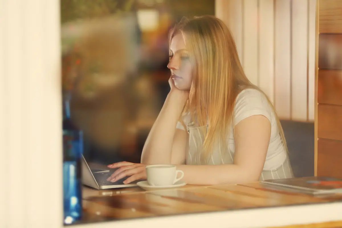Beautiful young woman with laptop in cafe view from outside