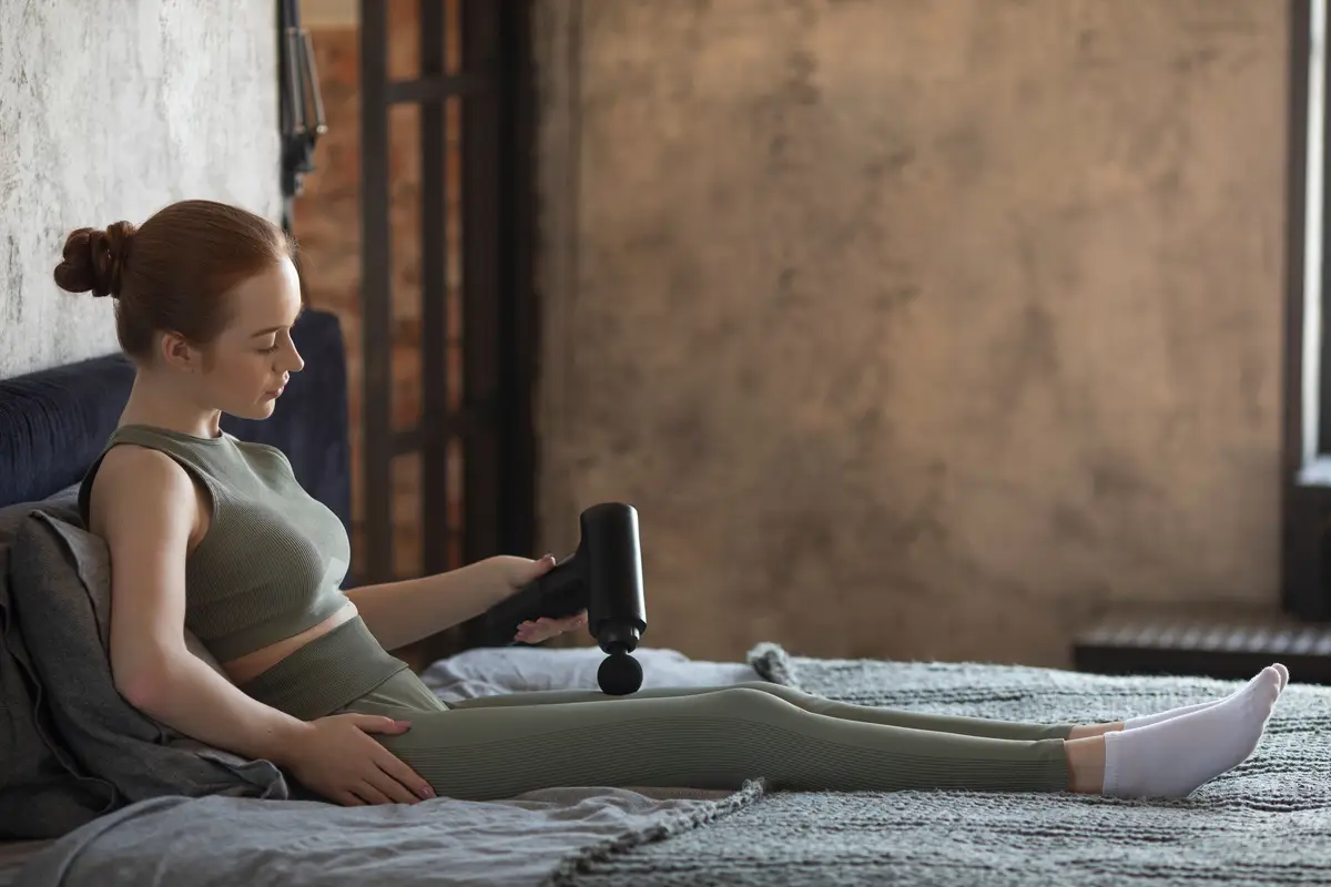 Full shot woman using massage gun on leg