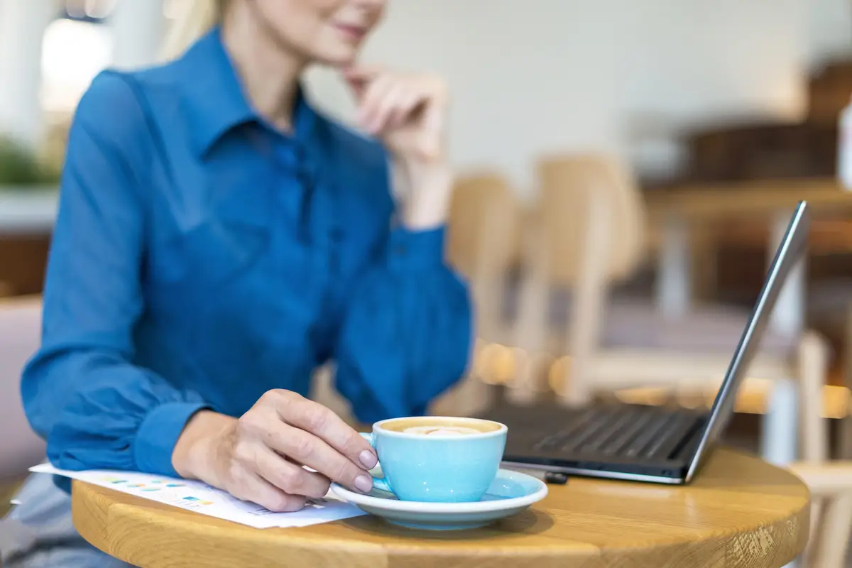 Side view of defocused older business woman having coffee while working on laptop