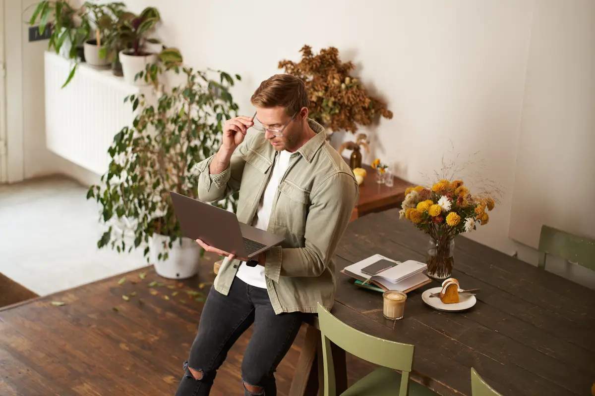 Handsome manager man in glasses sits on table holds laptop and types sends message works on project