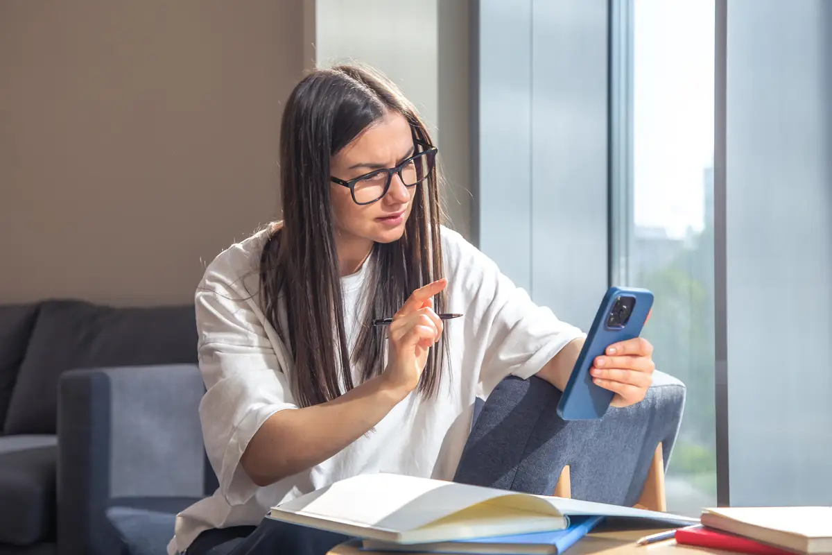 Student woman with smartphone and notepads at the window in the morning