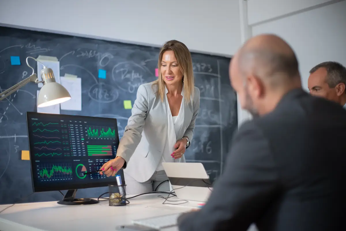 Company employees discussing market data on charts. Skilled woman leader and two men looking at diagrams on computer screen analyzing profit growth. Business growth and female business leaders concept